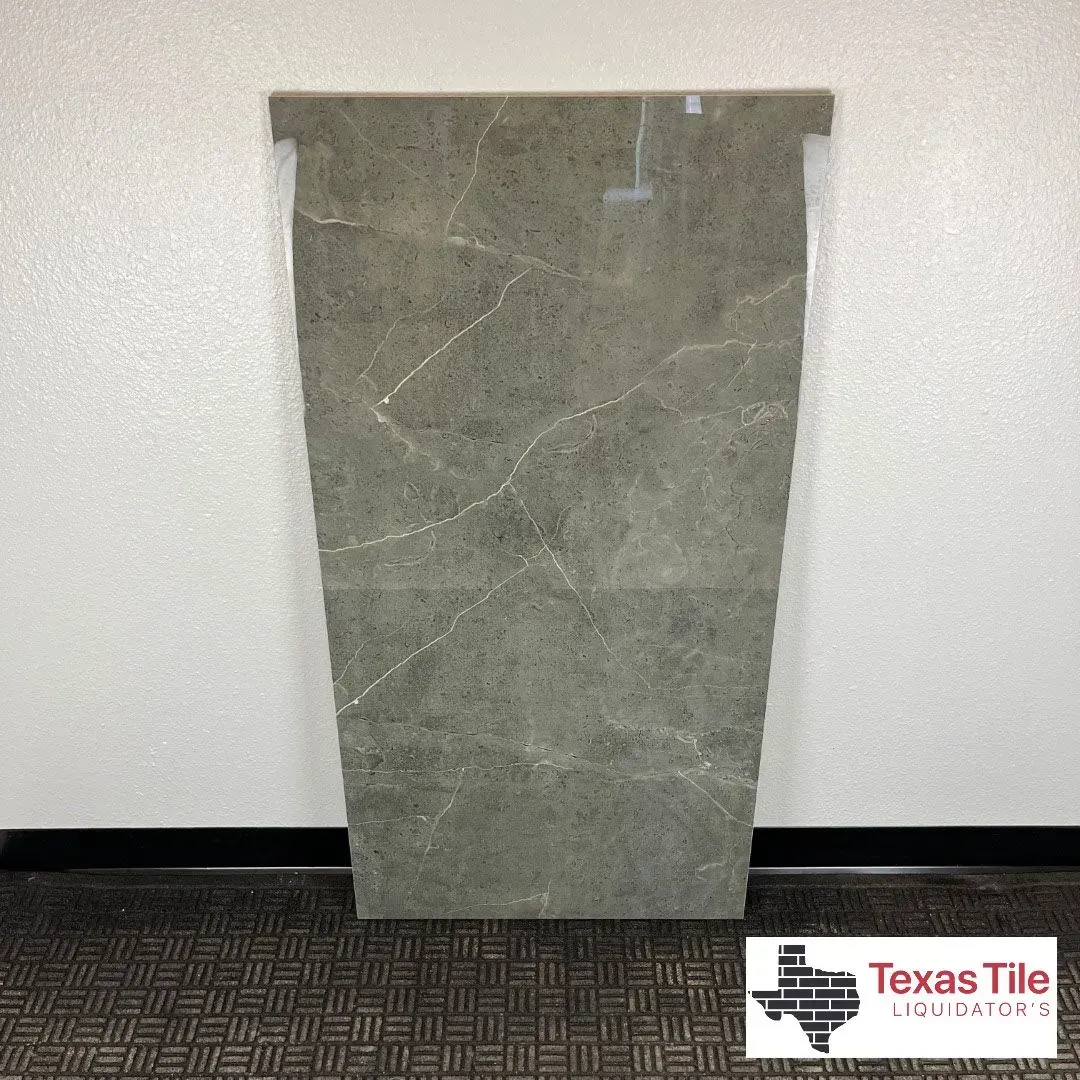 A rectangular, grey tile with subtle white veining displayed against a white wall with a Texas Tile logo in the corner.