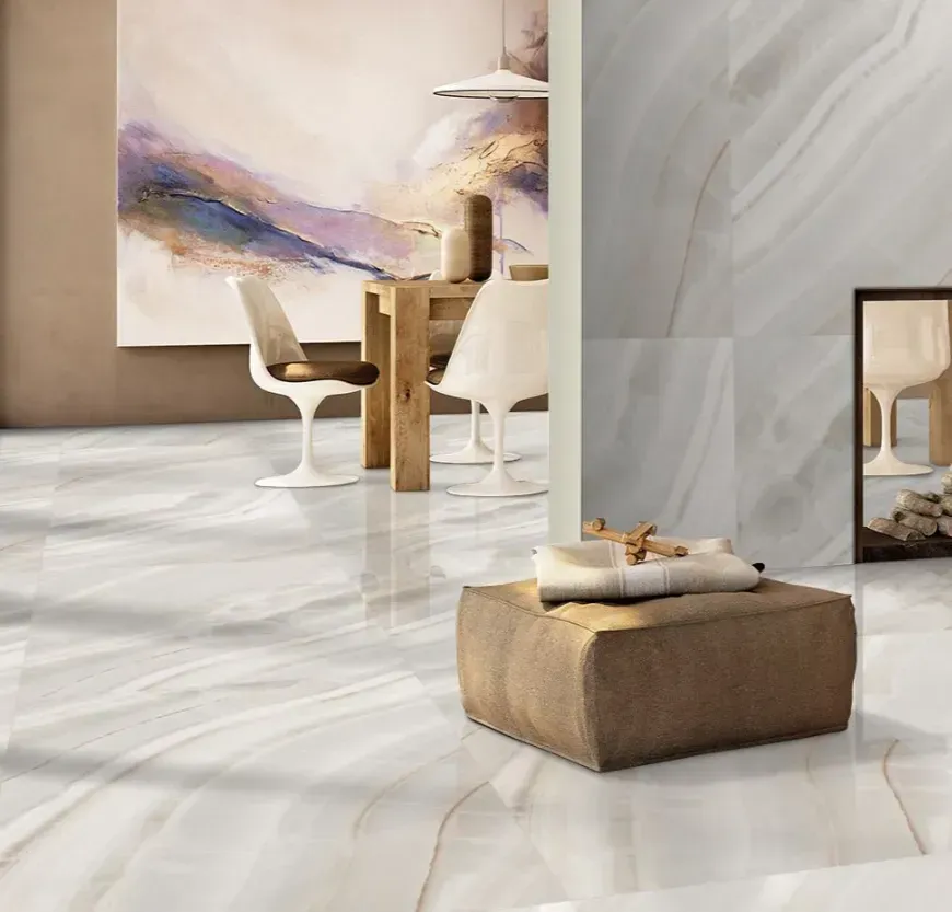 A modern interior featuring polished white marble flooring, a dining set, abstract wall art, and a brown ottoman.