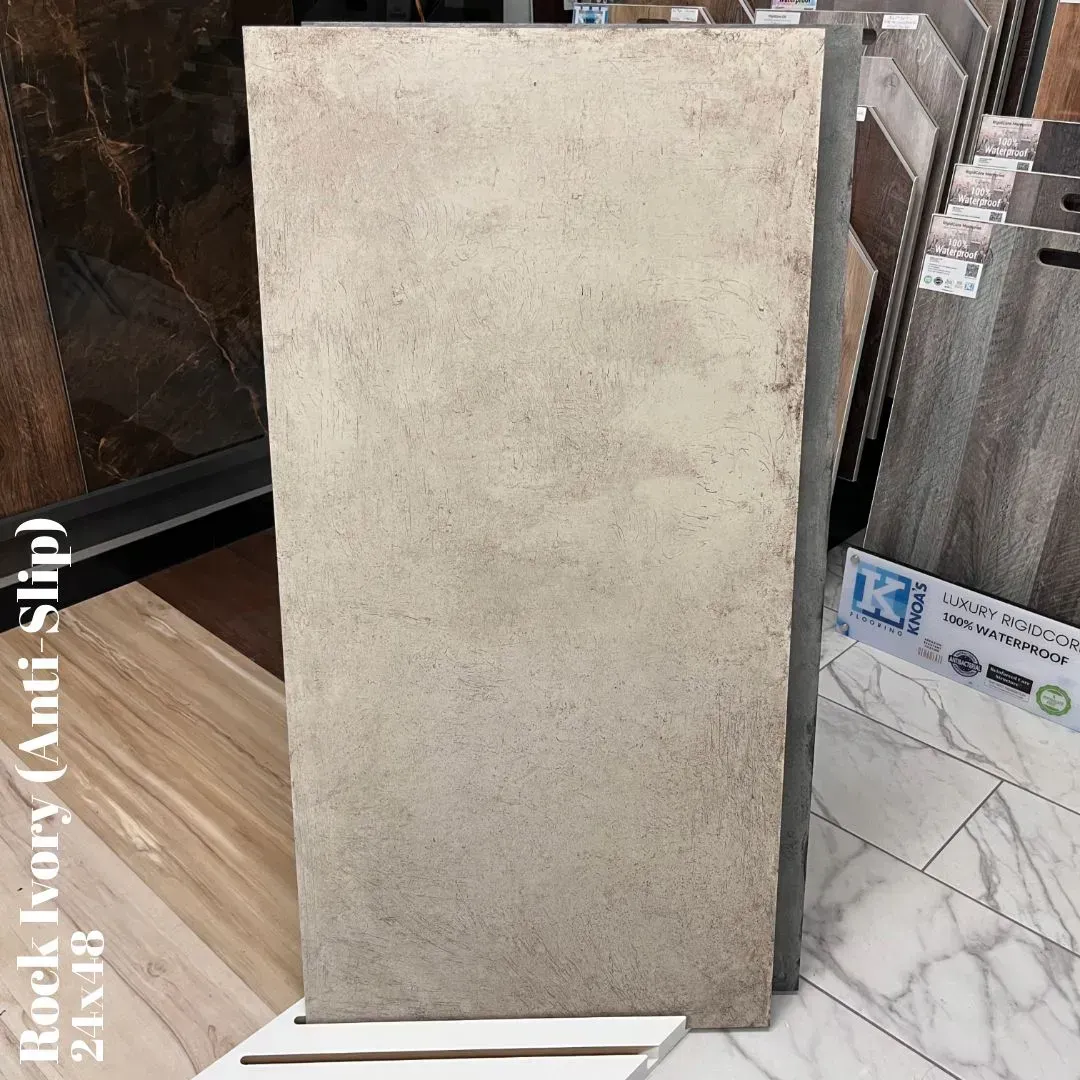 A single 24x48-inch Rock Ivory anti-slip tile on display in a showroom, featuring a textured, light beige concrete look.