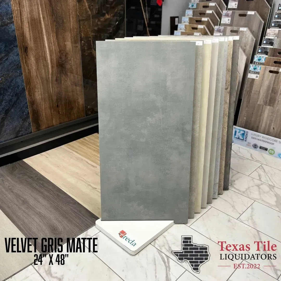 A gray Velvet Gris Matte tile sample displayed on a rack at Texas Tile Liquidators, with other tile options in the back.