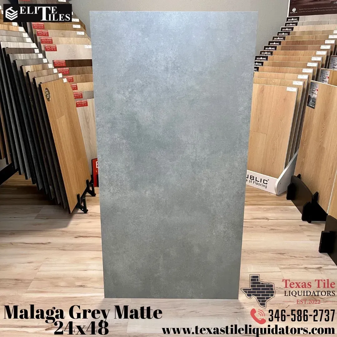 A grey matte 24x48 Malaga tile displayed in a showroom with wooden flooring and tile samples in the background.
