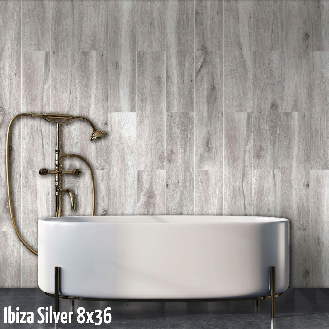 A white freestanding bathtub set against a wall with vertical light grey, wood-look plank tiles and antique brass fixtures.