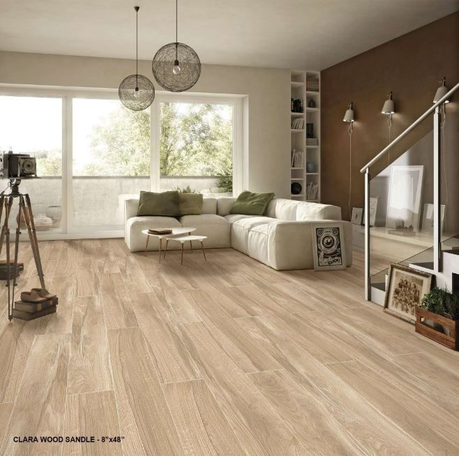 A bright living room with light wood-look floor tiles, a white sectional sofa, and pendant lighting.