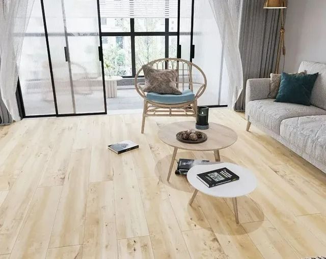 A bright living room with light wood floors, a rattan chair, two small round coffee tables, and a grey sofa.
