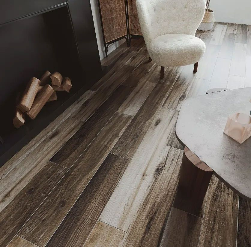 A modern interior with wood-look flooring, a fireplace containing logs, a white armchair, and a stone coffee table.