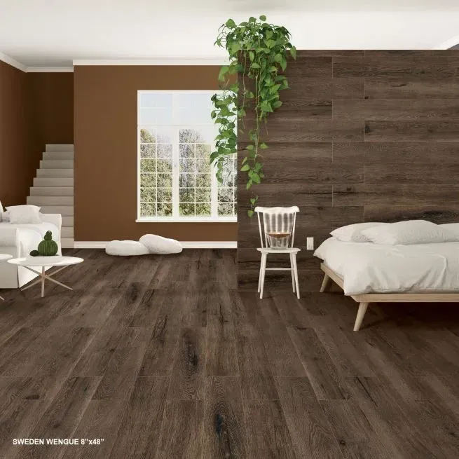 A bedroom with dark wood flooring and a matching wood-paneled accent wall, a white bed, a chair, and a hanging green plant.