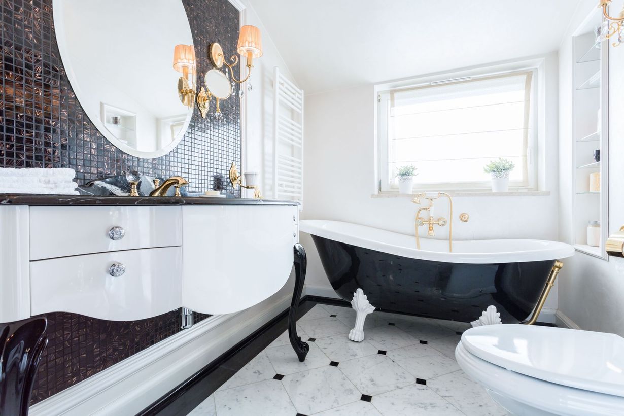 A luxurious bathroom featuring a black and white clawfoot tub, a modern white vanity, and a black mosaic tile wall.