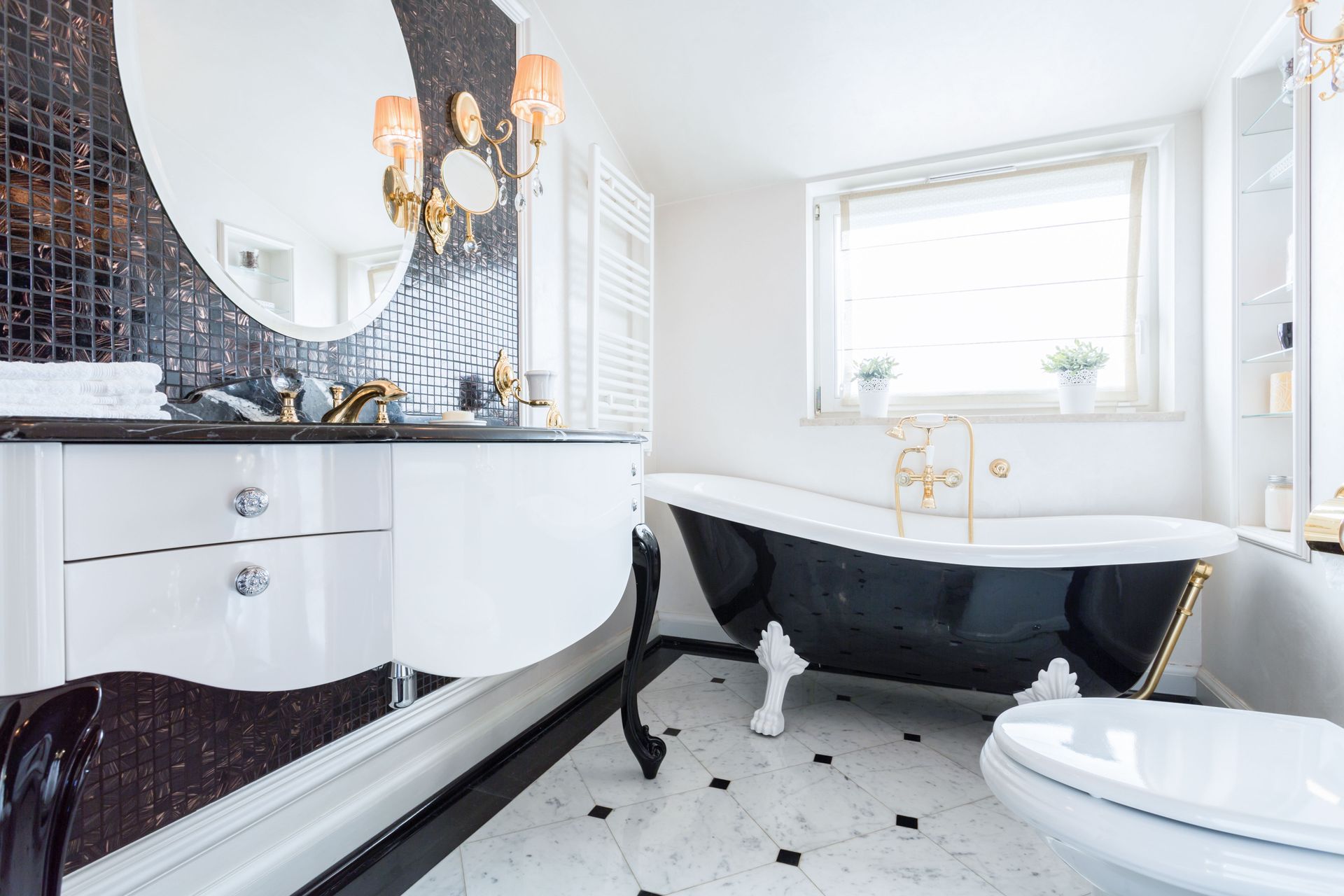 A luxurious bathroom featuring a black and white clawfoot tub, a modern white vanity, and a black mosaic tile wall.