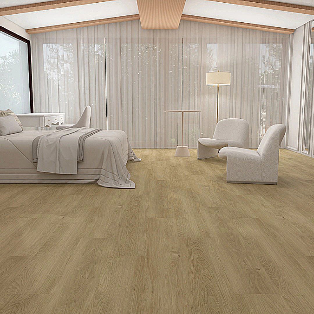 A bedroom with light wood flooring, a bed, two armchairs, sheer floor-to-ceiling curtains, and a floor lamp.