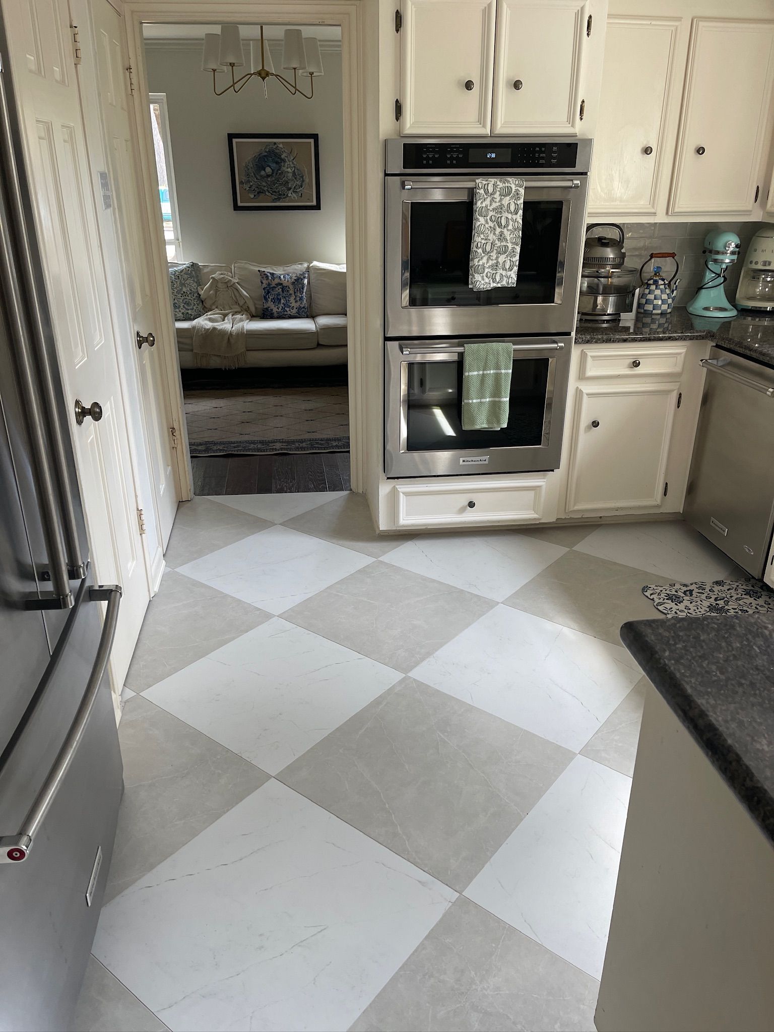 A white-and-gray checkered tile kitchen floor leads to a doorway showing a living room with a sofa.
