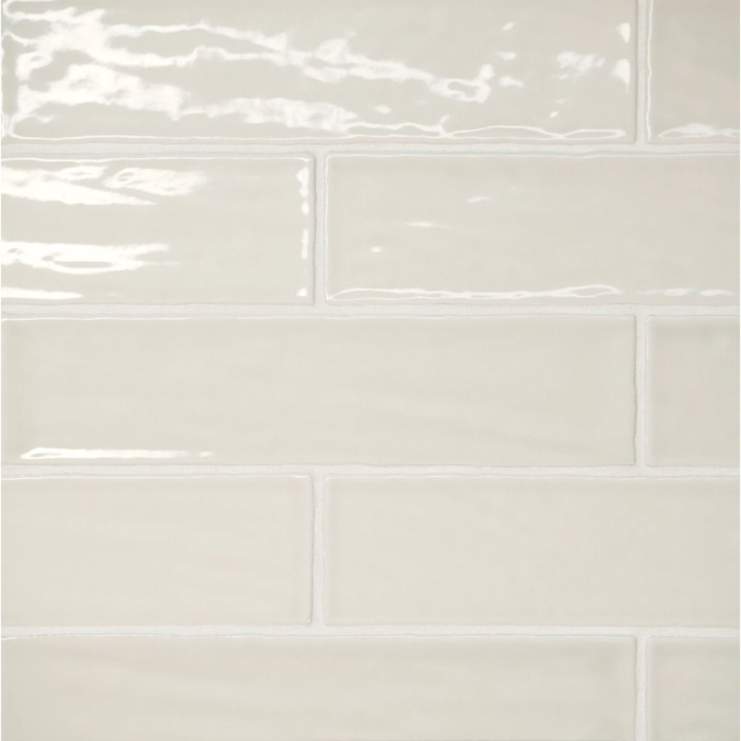 A wall covered in glossy, off-white rectangular subway tiles with a slightly uneven, handmade aesthetic.