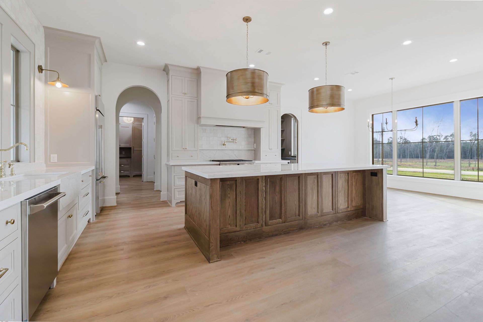 Modern kitchen with a wooden island, white cabinetry, farmhouse sink, and hanging pendant lights overlooking a yard.