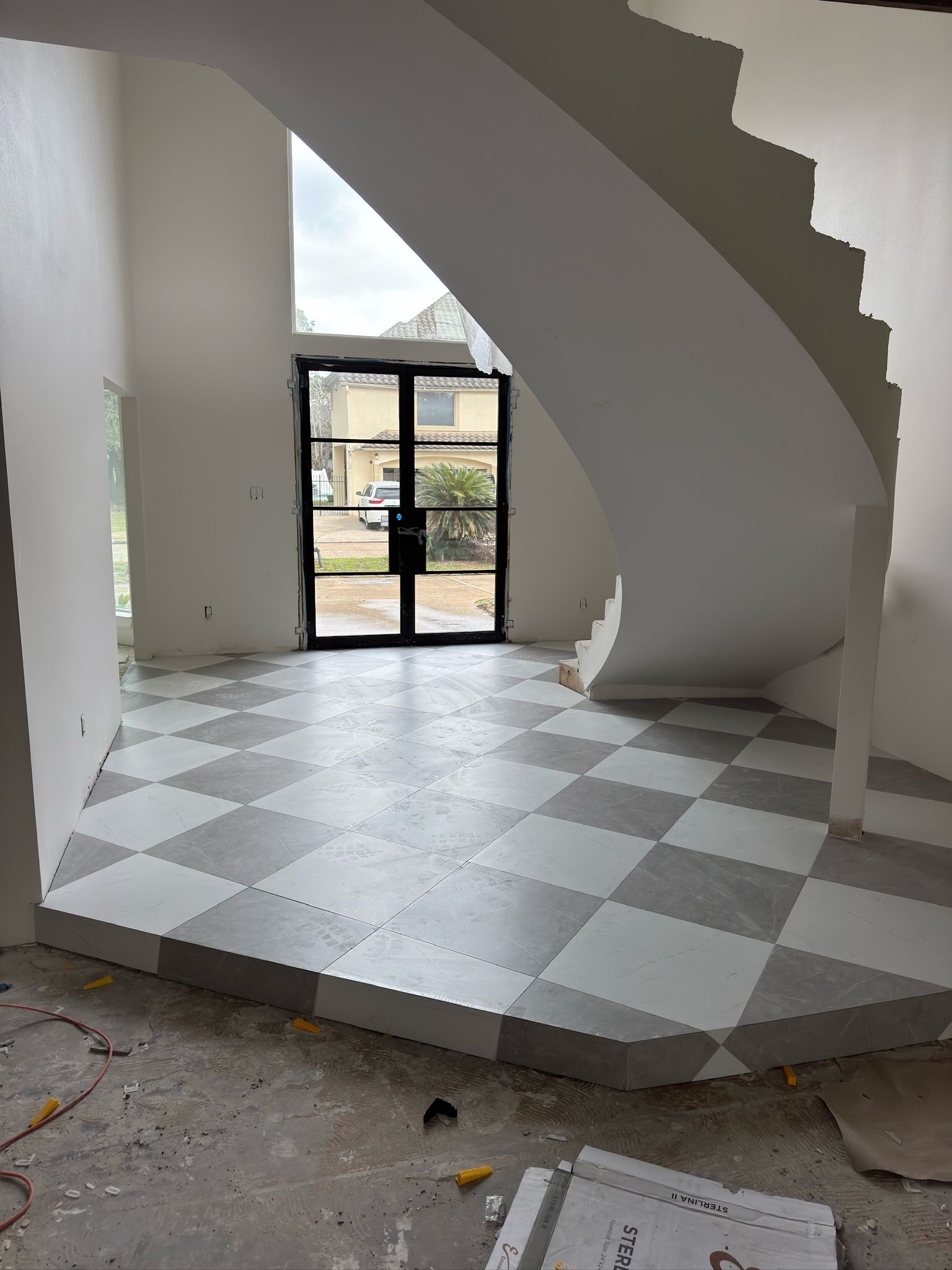 A modern entryway with a raised, gray and white checkered floor, a curved staircase, and large black-framed glass doors.
