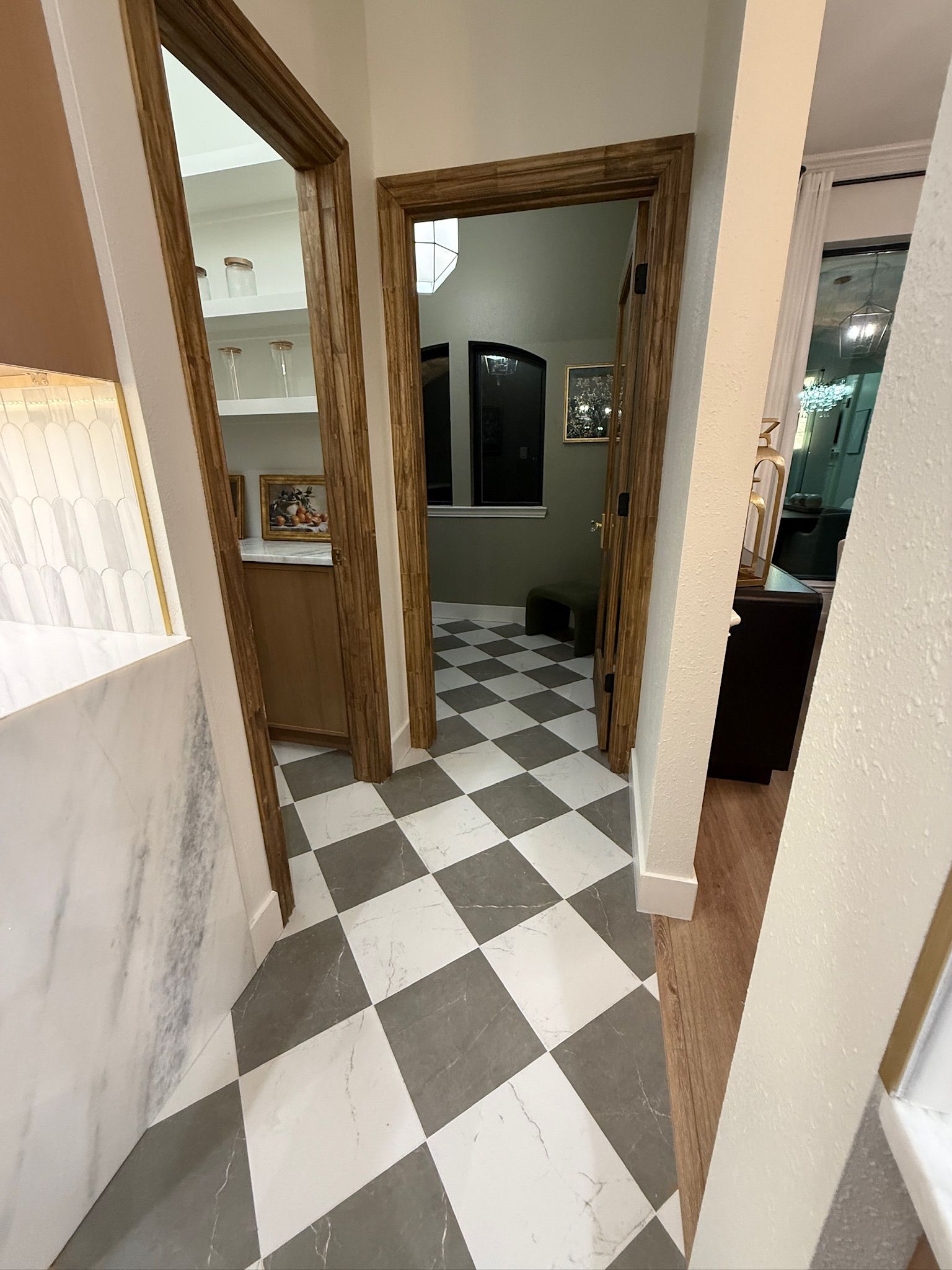 A perspective view of a home interior featuring checkered floor tiles and two doorways with wooden trim.