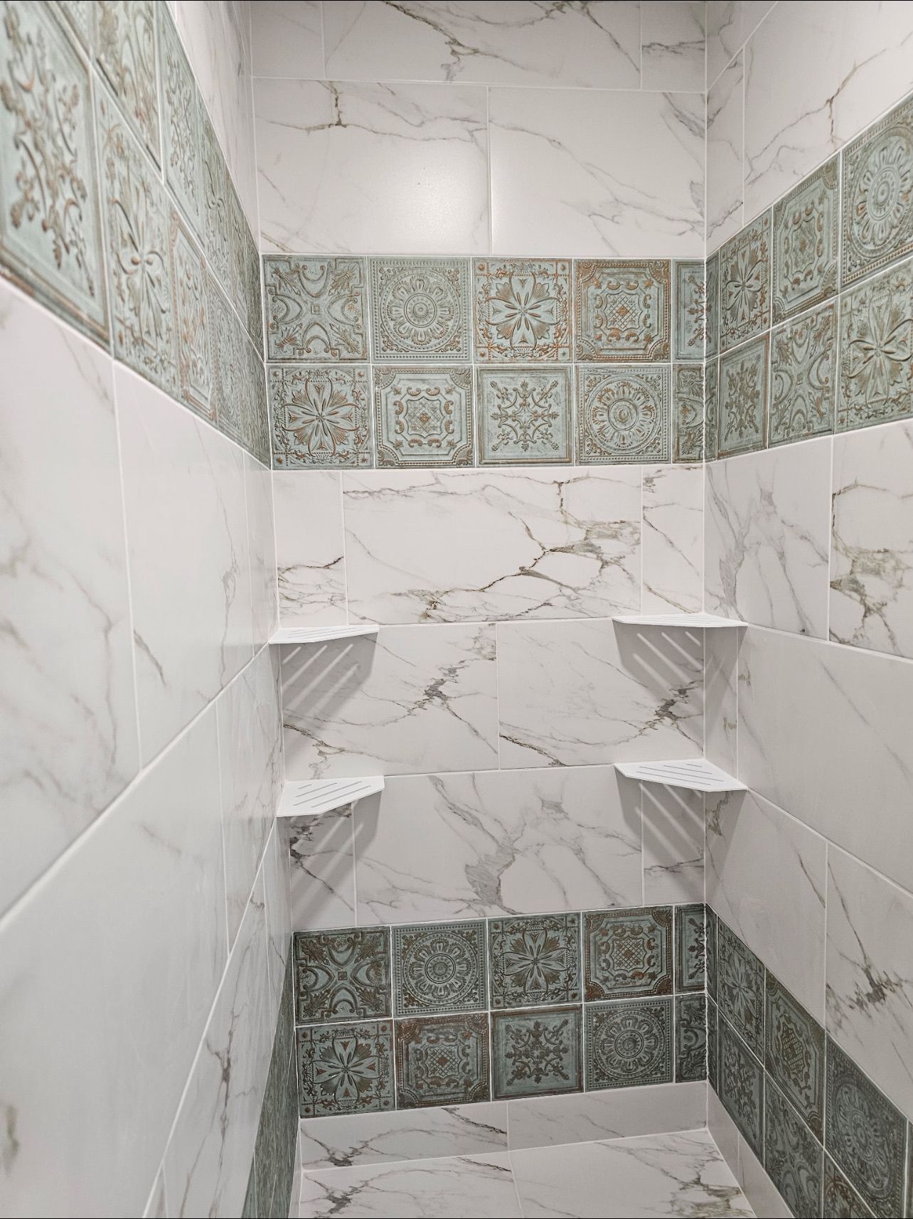 A shower interior featuring white marble-patterned tiles accented by rows of decorative green and white patterned tiles.
