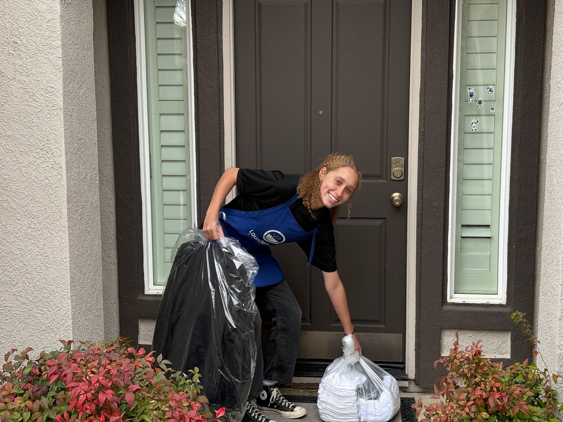 A woman is standing in front of a door holding a bag of clothes.