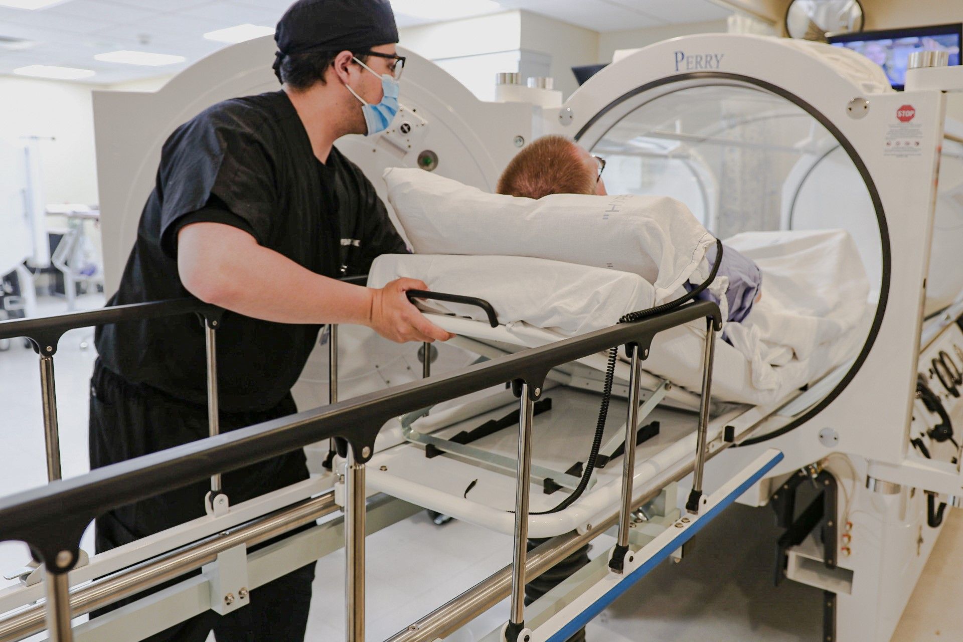 Technician pushing a patient on a stretcher into an MRI scanner in a hospital room