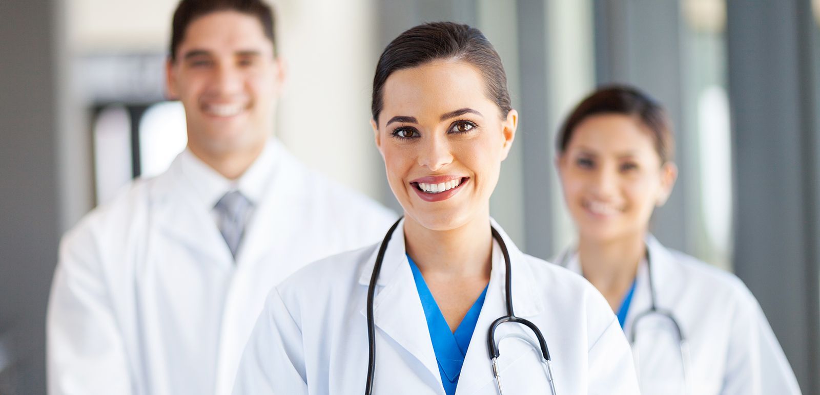 Three smiling medical professionals in white coats in a bright hospital hallway