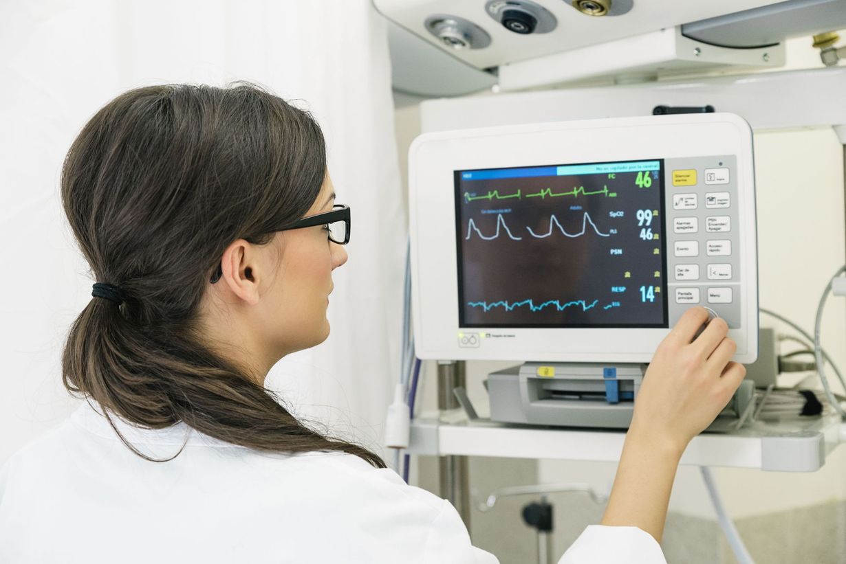 Clinician adjusting a hospital vital signs monitor showing patient waveforms