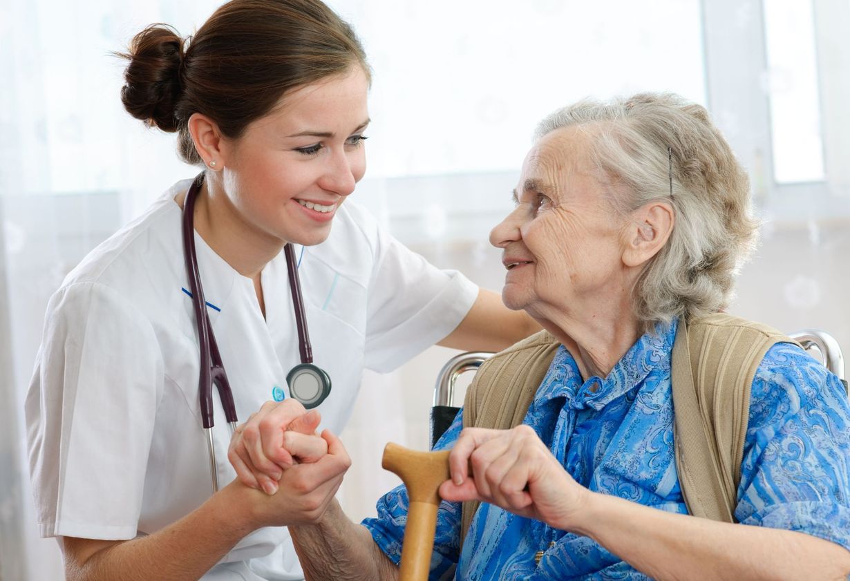 Nurse smiling and holding hands with an elderly patient in a bright clinic room