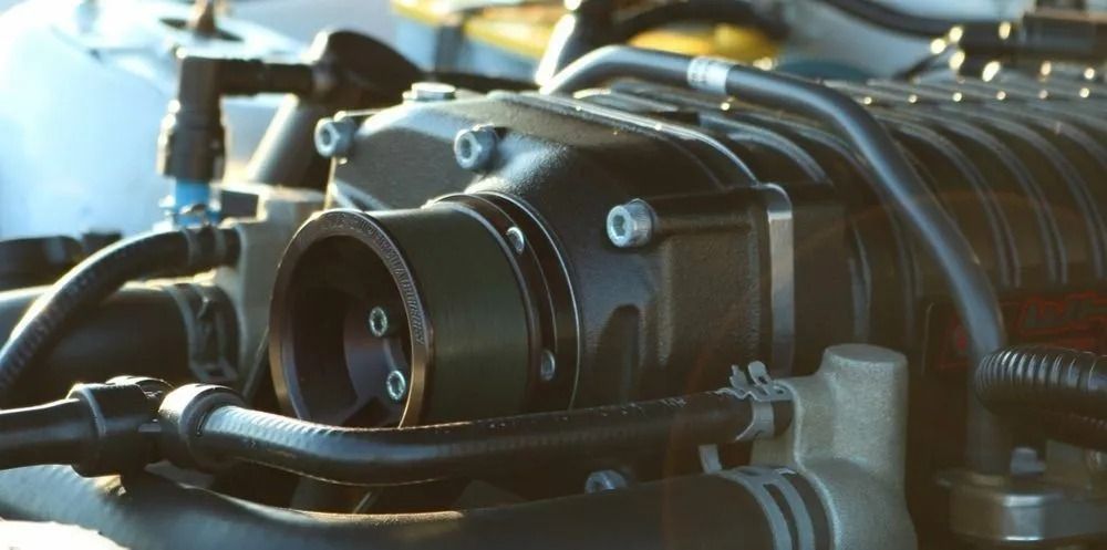 Close-up of a car engine component with black hoses and metal fittings under warm light