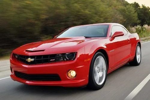 Red sports car driving on a road with trees in the background