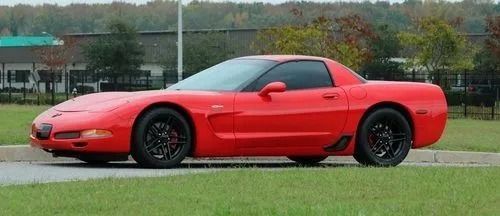 Red sports car parked on grass, side view, with black wheels and overcast sky