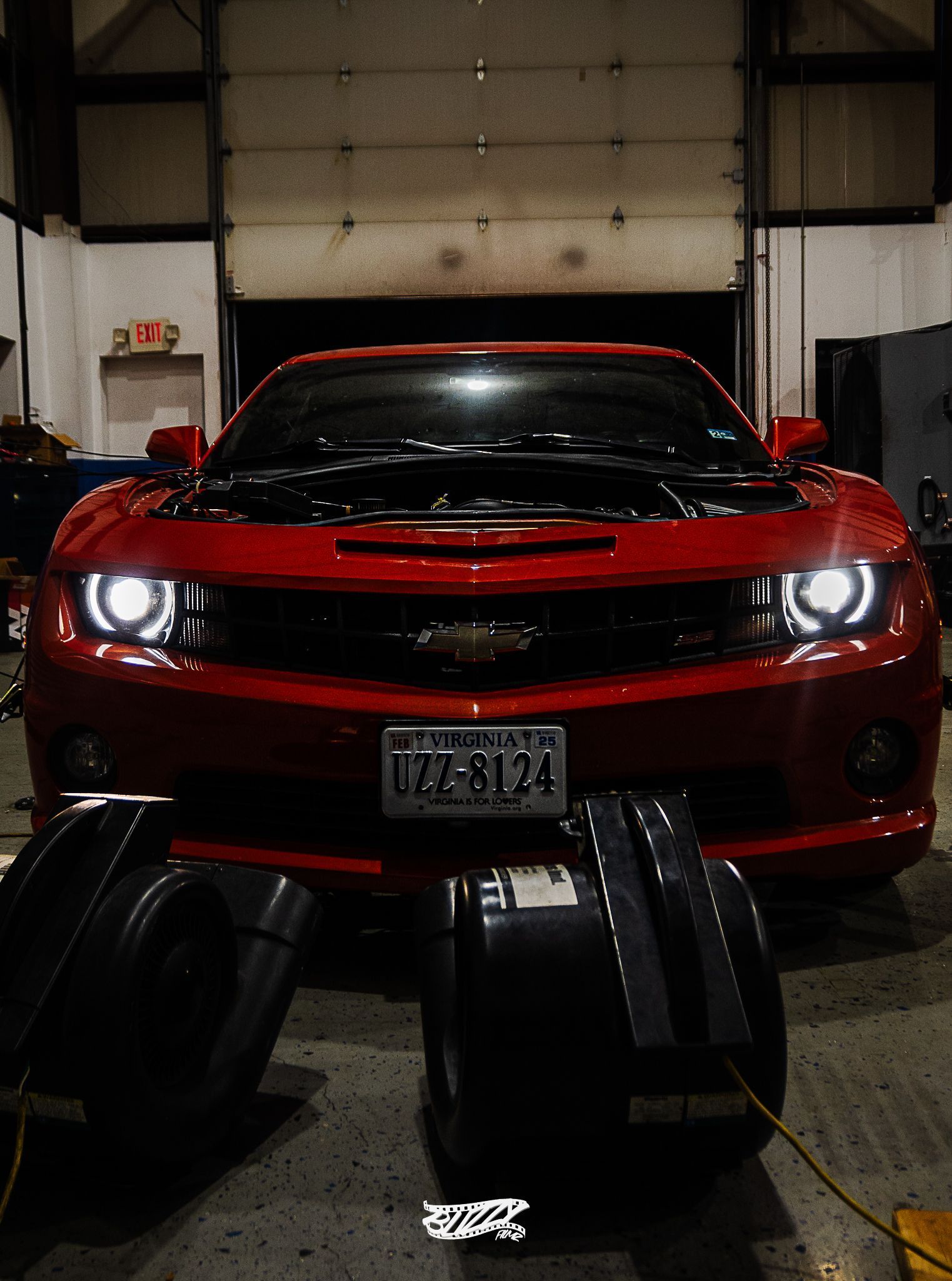 Red sports car with headlights on in a garage, viewed from the front.