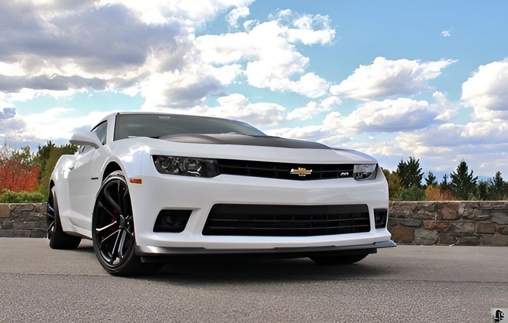 White Chevrolet Camaro parked on a road with a stone wall and cloudy sky in the background
