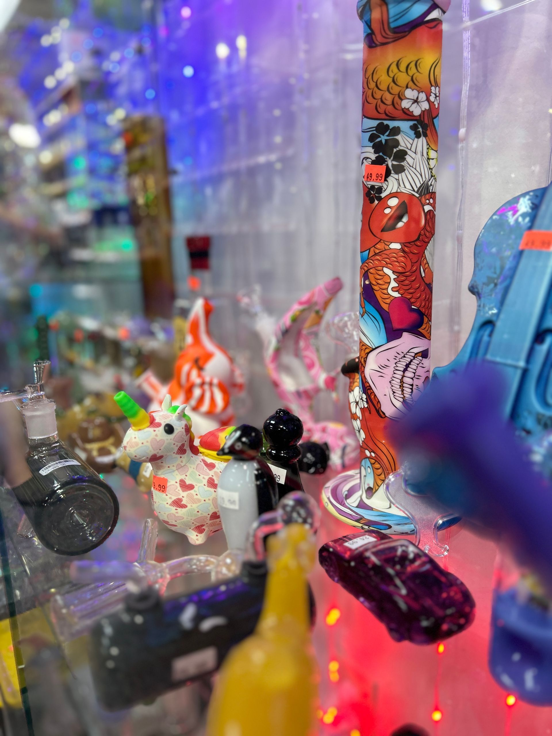Glass smoking pipes in a brightly lit display case; various colors and shapes, including a unicorn and car.