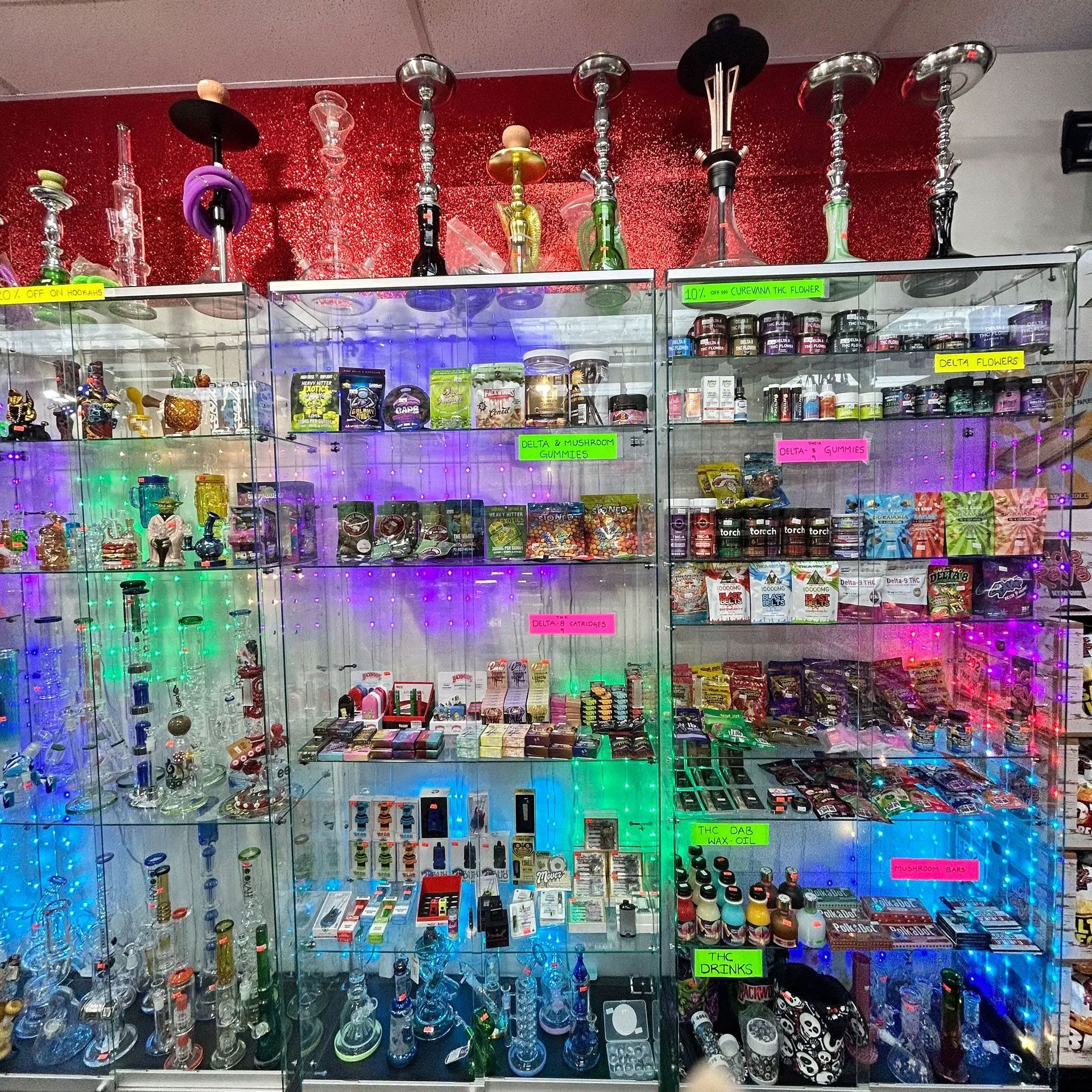 A store display with glass pipes, bongs, and smoking accessories, lit by colorful LED lights.