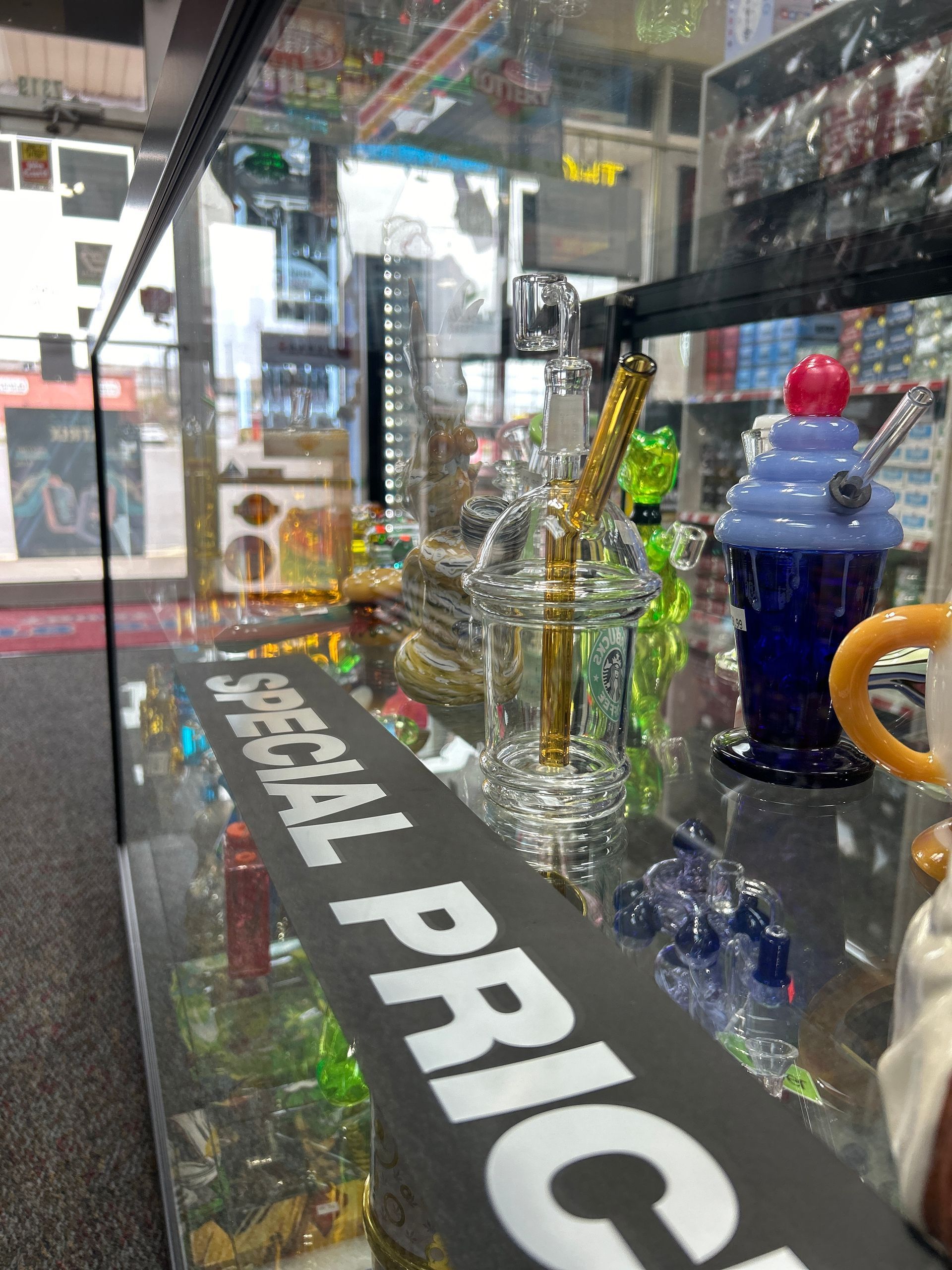Glass display case with smoking pipes, including a beaker-style piece, and a blue and purple piece, in a shop. 