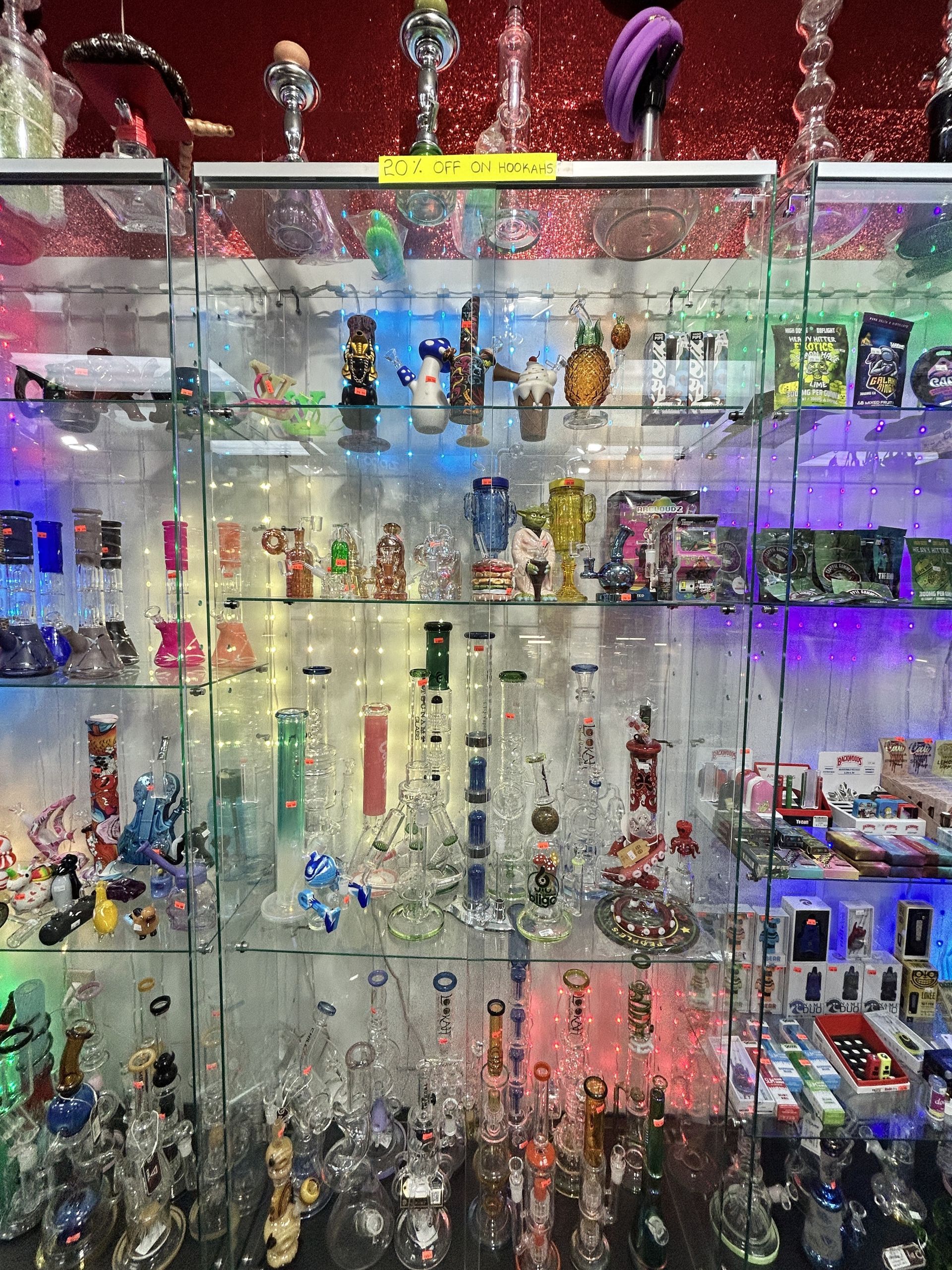 Glass bongs and other smoking accessories displayed in a glass cabinet with colorful LED lighting.