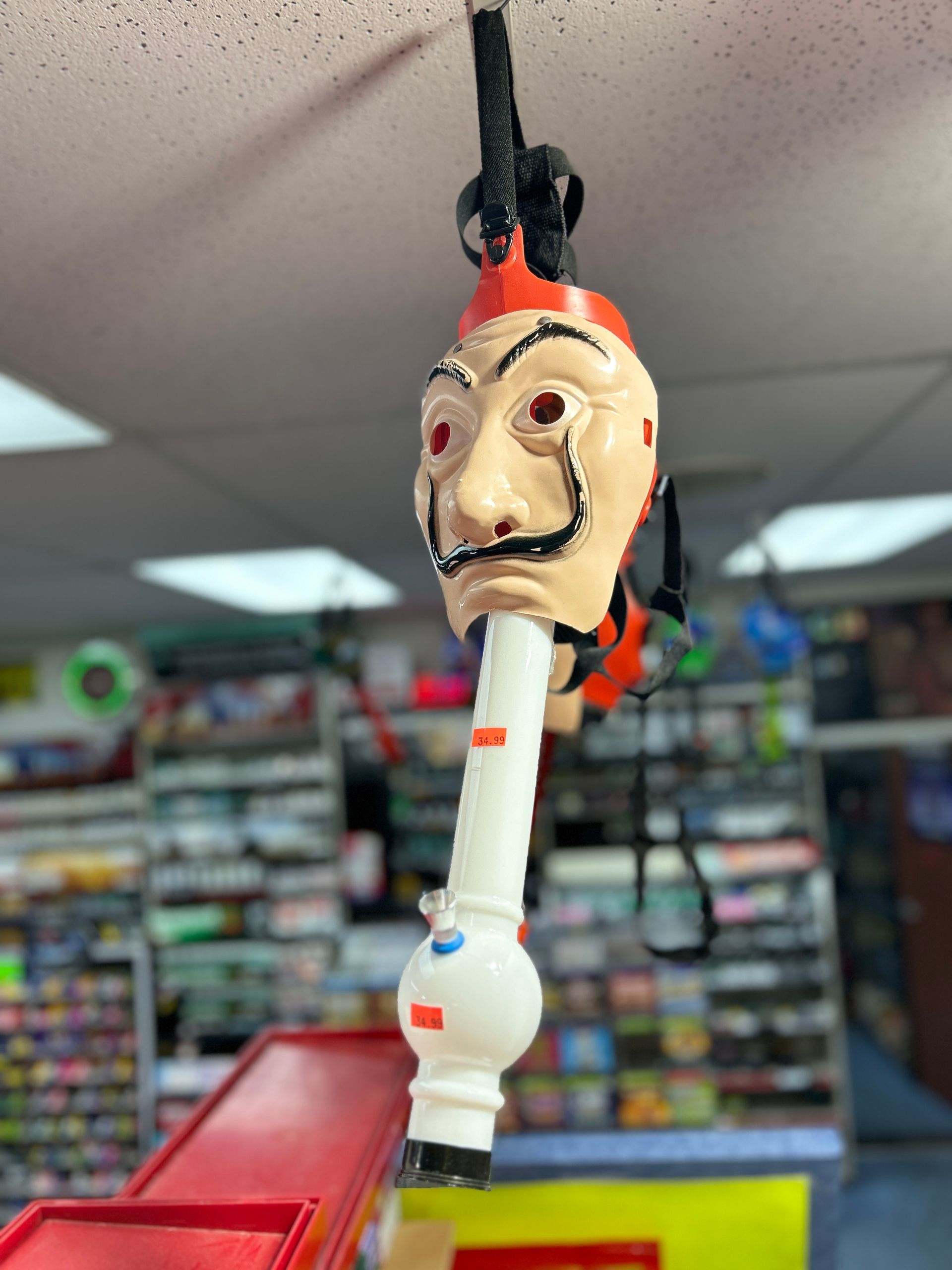 Bong decorated with a Dali mask, hanging in a store. White, orange, and black colors are visible.