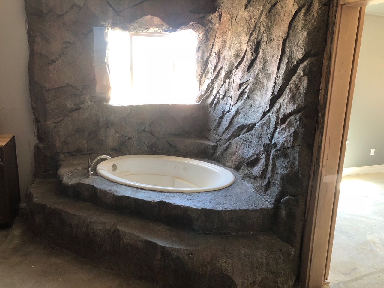 A bathroom with a jacuzzi tub surrounded by rocks and a window.