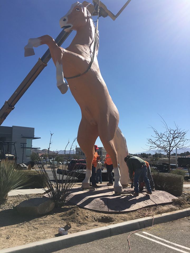 A statue of a horse is being lifted by a crane.