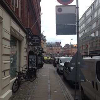 Sidewalk with shops and parked vehicles on a city street. Grey sky.