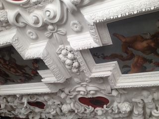 Ornate white ceiling with painted figures, intricate carvings, and red accents.