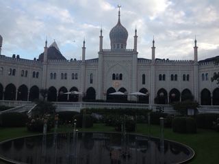 White, ornate building with a central dome, spires, and a reflective pool in a garden; cloudy sky.