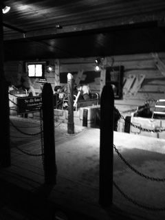 Black and white interior with wood beams, posts, chains, and a small lit window.