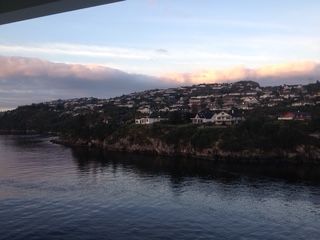 Coastal town at dusk, houses on a hillside, calm water, and a cloudy sky.