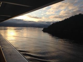 Sunset over water from a ship, with a silhouetted coastline on the right.