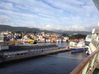 Harbor view of Bergen, Norway with buildings, boats, and a cruise ship. Blue sky and water.