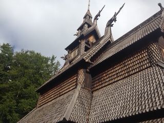 Wooden stave church with ornate roof and gables, against a cloudy sky and trees.