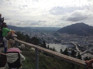 People overlooking a city from a mountain viewpoint with a wooden railing.