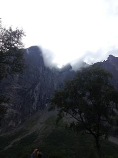 Mountain landscape with clouds partially obscuring the peaks. Trees frame the view.