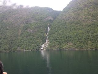 Waterfall cascading down a lush, green mountainside into a dark body of water.