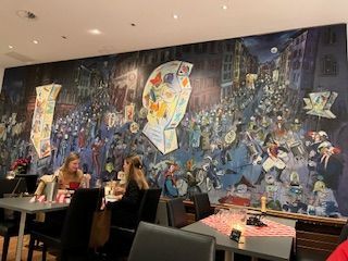 Restaurant interior with diners and a large mural depicting a nighttime street festival with lanterns.