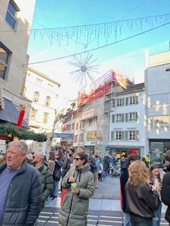 Crowded city street with pedestrians, buildings, and holiday decorations overhead.