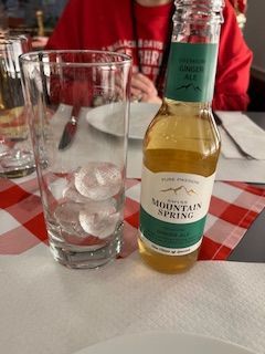 A glass with ice next to a Mountain Spring ginger ale bottle on a checkered tablecloth.